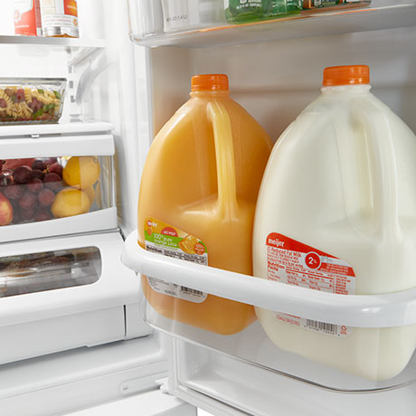 Large storage bins holding a gallon of orange juice and a gallon of milk.
