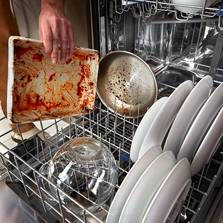 Man's hand placing dirty casserole dish in lower rack.
