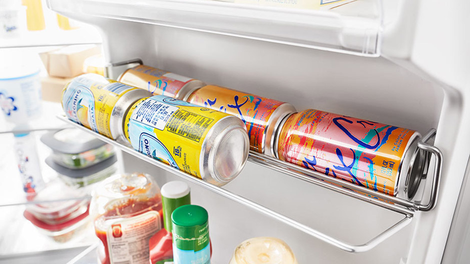 Five cans of soda neatly stored in the refrigerator door with space for one more.